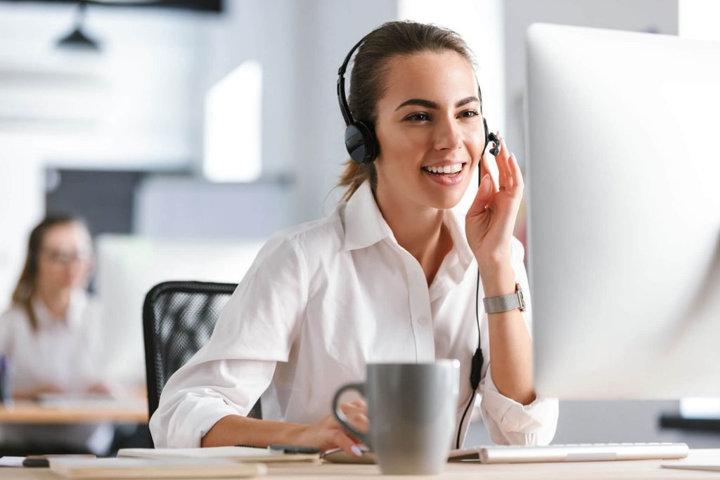 Claims agent smiling at her desk while assisting customer over the headset.